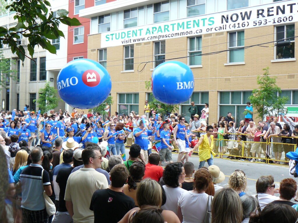 Introduction to Queer Canada: 30 Days of Stories 2 BMO marchers in the Toronto Pride Parade from 2008. There are two large BMO balloons overhead.